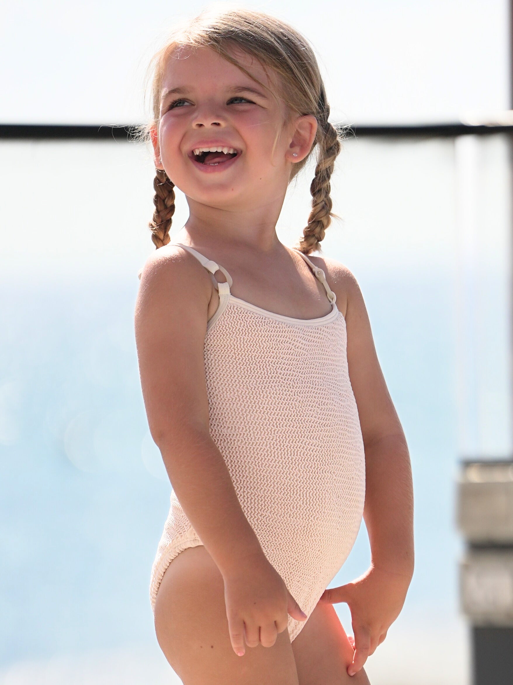 Coco Kids one-piece swimsuit in sand on a child model, showing textured fabric and slim straps