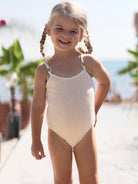 Coco Kids one-piece swimsuit in sand on a child model, showing textured fabric and slim straps